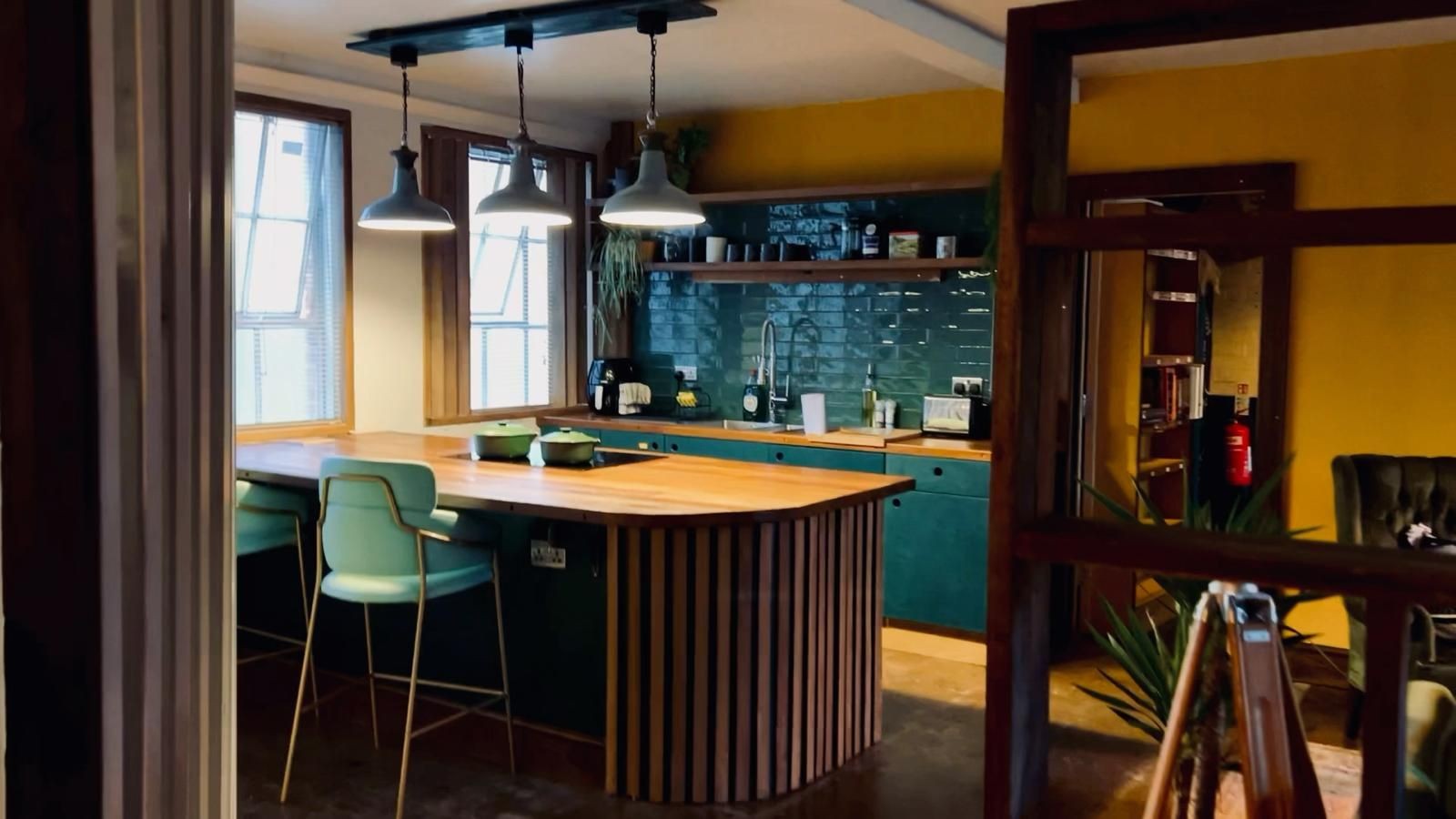 Cozy kitchen with teal cabinetry, wooden island, and green chairs under pendant lights.