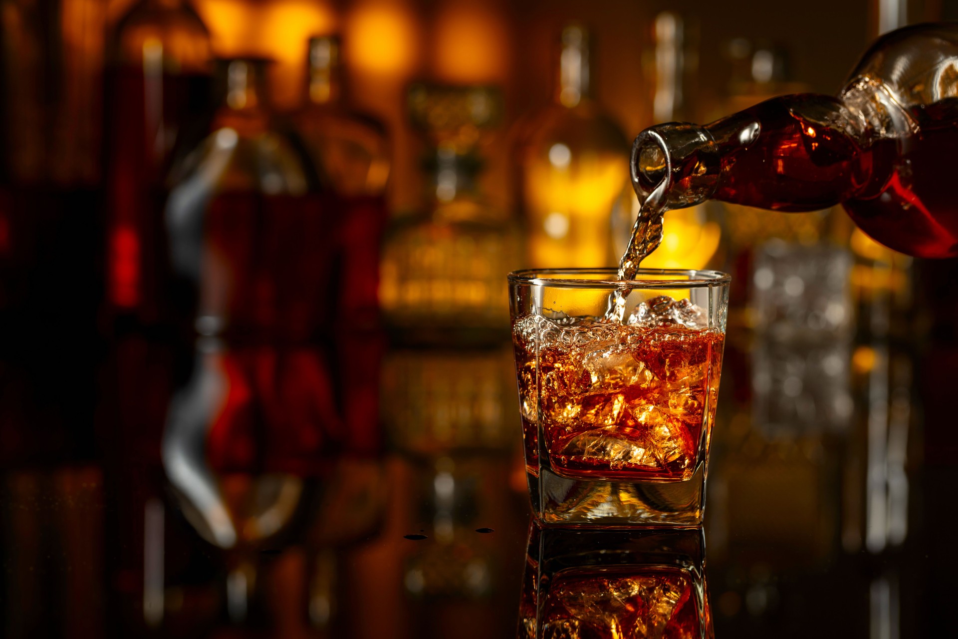 Whiskey is poured from a bottle into a glass with ice.